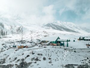 Aerial view of Gulmarg ski resort with snowy mountains, vibrant buildings, and people enjoying winter activities.